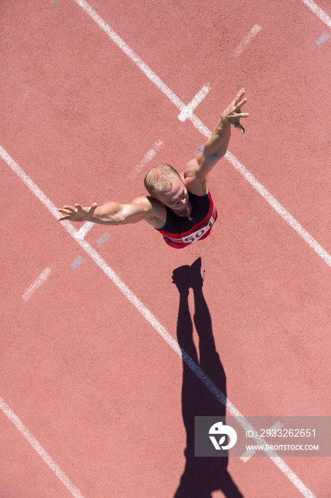 Male track and field athlete jumping on sunny running track