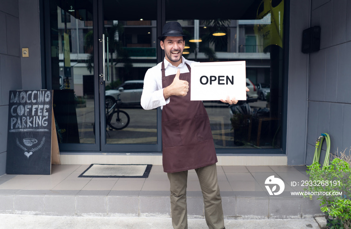 Portrait of a happy waitress standing at coffee shop entrance and holding open sign in front coffee 