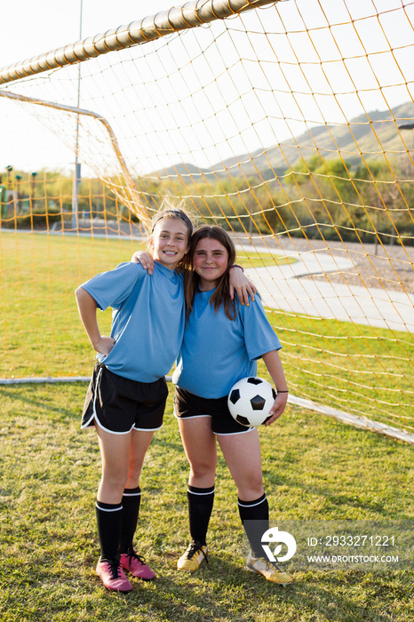 Portrait of smiling girls with ball standing on soccer field against net