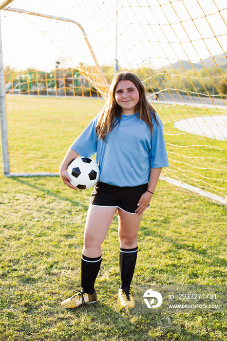 Portrait of smiling girl holding soccer ball near goalpost