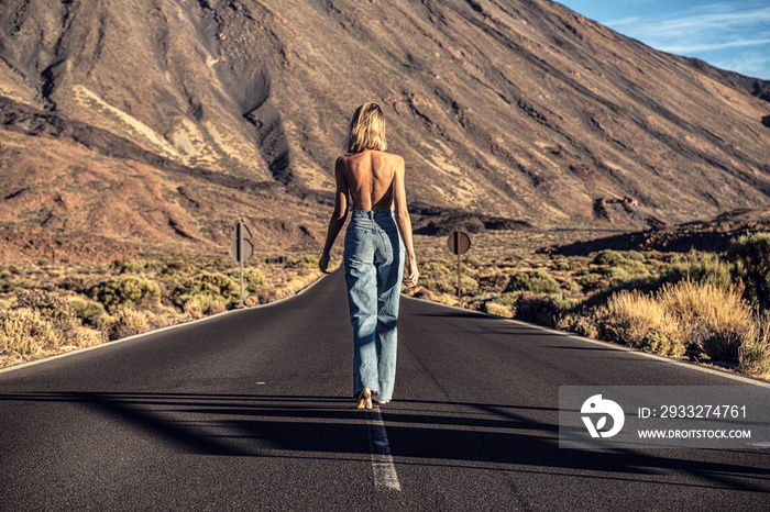 Woman topless traveler in jeans walking away on the street over the wild mountains landscape. Back v