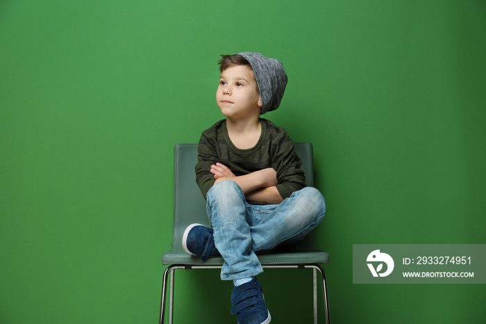 可爱时尚的男孩坐在靠近彩色墙的椅子上