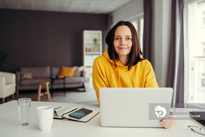 Portrait of confident female professional sitting with laptop at home office