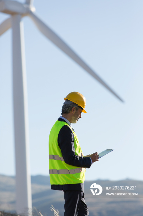 Male engineer examining wind turbine on sunny wind farm