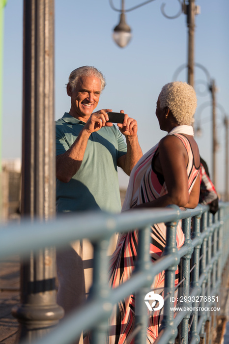 Senior man photographing wife on sunny pier