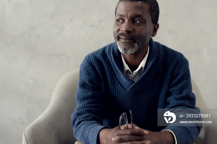 mature african american man sitting on armchair and holding eyeglasses