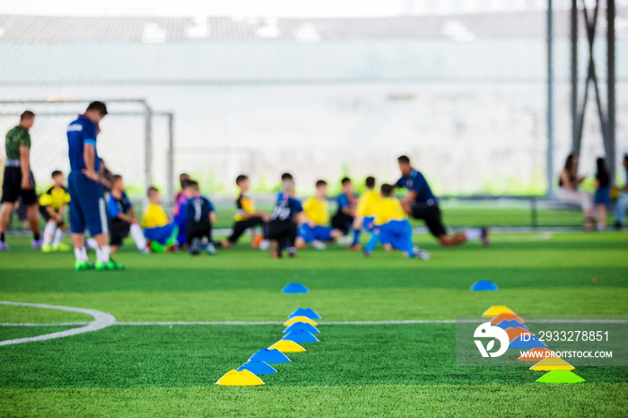 Cone markers is soccer training equipment on green artificial turf with blurry kid players training 