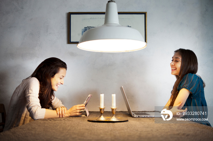 Two girl friends sitting at table using tablet pc and laptop