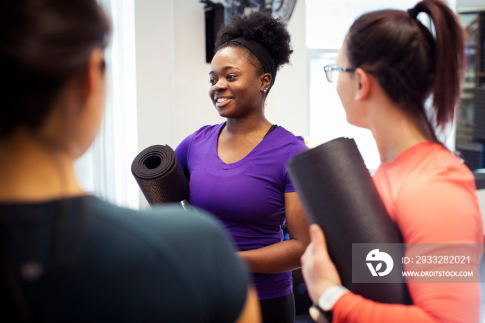 Smiling female athletes with exercise mats talking while standing in yoga class