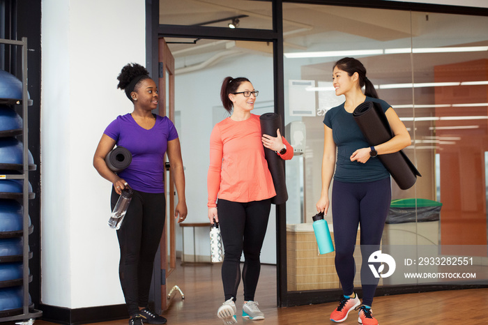 Female athletes with exercise mats and water bottles talking while entering in yoga class