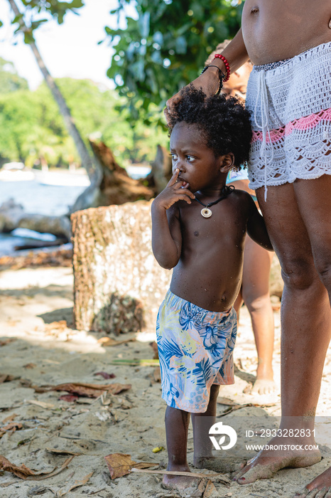 Imagen vertical de un pequeño niño afroamericano con cabello afro y sin camisa en la playa de pie al