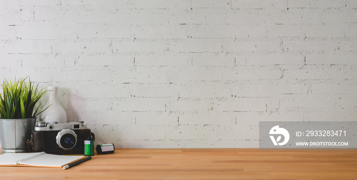 木桌子和砖墙上摆放着相机和办公用品的舒适工作场所的裁剪镜头