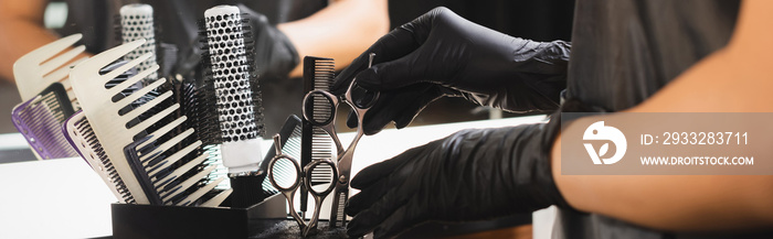 partial view of barber in latex gloves putting scissors in holder, banner