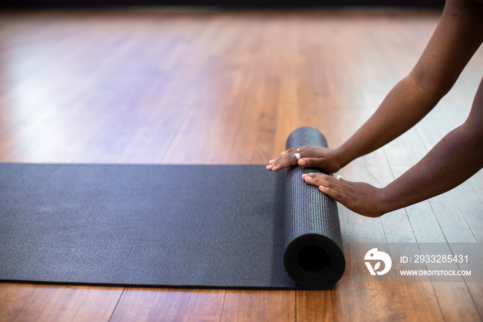 Cropped hands of athlete rolling exercise mat on hardwood floor in gym