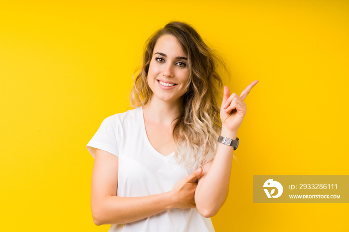 Young beautiful blonde woman over yellow background with a big smile on face, pointing with hand and