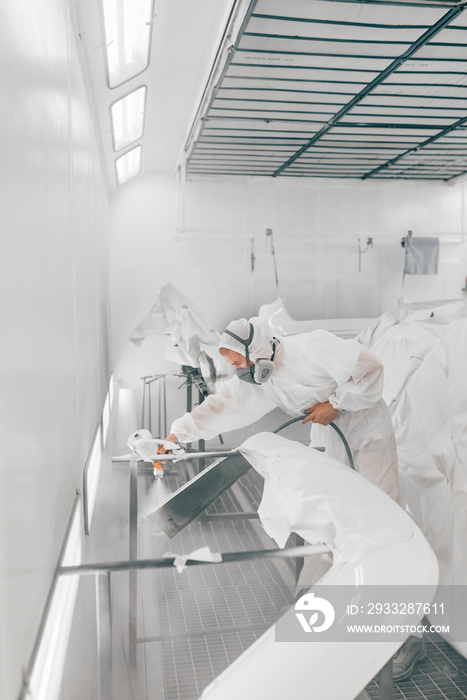 Worker spraying car parts with white paint.