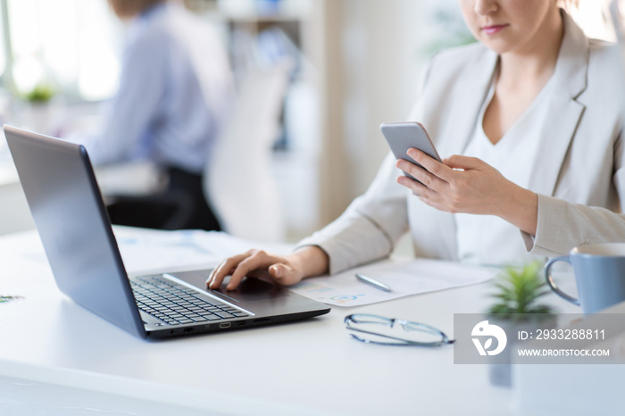 business, technology and people concept - businesswoman with smartphone and laptop computer at offic