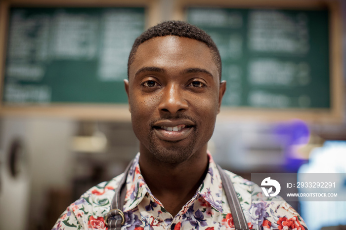 Close-up portrait of smiling male barista standing in coffee shop