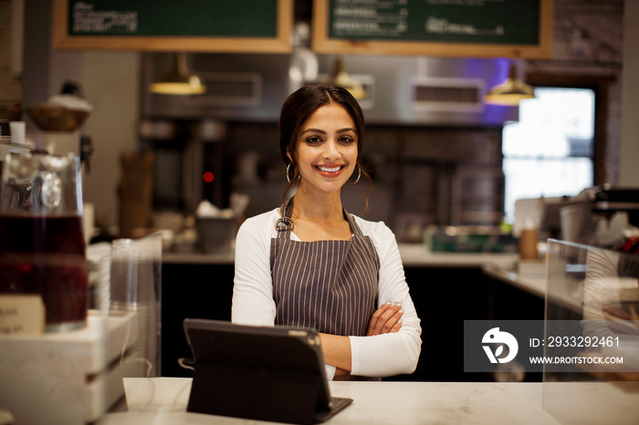 Portrait of smiling confident female manager with tablet computer on bar counter standing in cafe