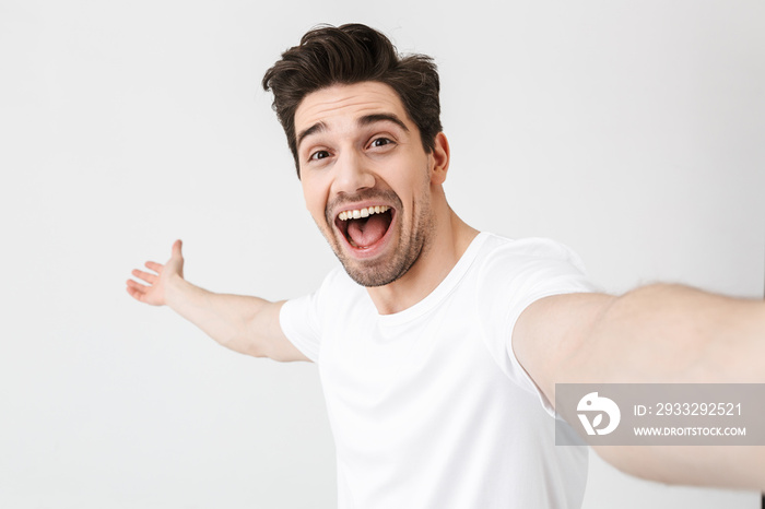 Excited happy young man posing isolated over white wall background make a selfie by camera.