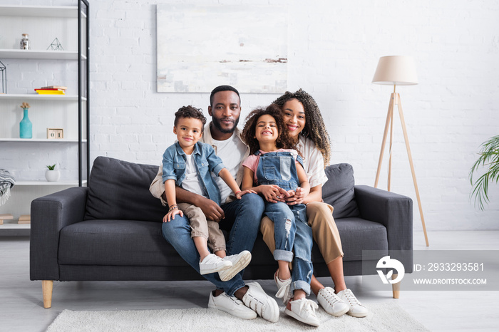 happy african american family sitting on sofa at home and looking at camera