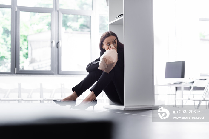 selective focus of young lecturer sitting on floor and hiding behind podium tribune, while suffering