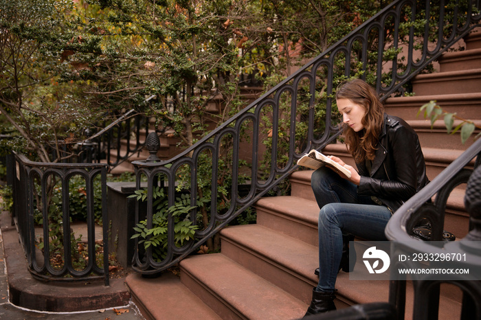 Young woman reading book while sitting on steps