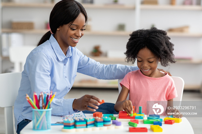 Pretty black kid and child development specialist playing with bricks