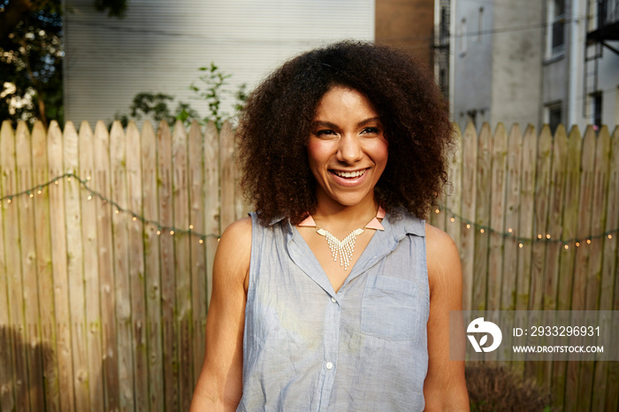 Young woman standing in front of garden fence, smiling