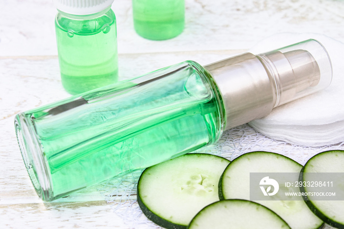 Liquid cosmetics skin care in a bottle and green cucumber with a slice of cucumber on a white wooden