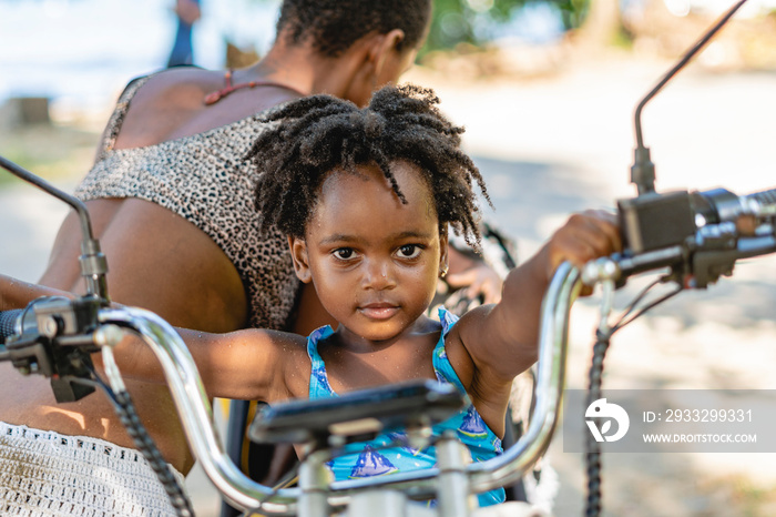 Imagen horizontal de una pequeña niña afroamericana mirando a cámara mientras se sostiene del manubr