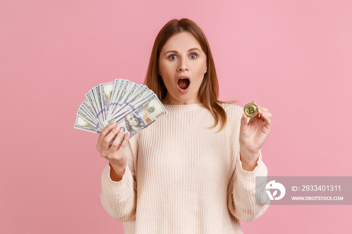 Amazed woman showing dollar bills and golden coin of crypto currency, transferring money into digita