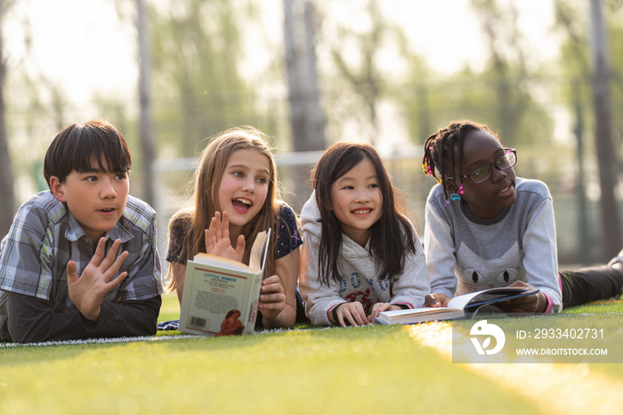 可爱的小学生们趴在草地上看书