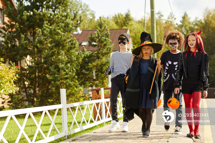 Full length portrait: group of children trick-or-treating wearing Halloween costumes while walking i