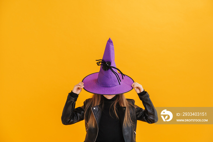 White girl wearing witch costume hiding into hat while posing at camera