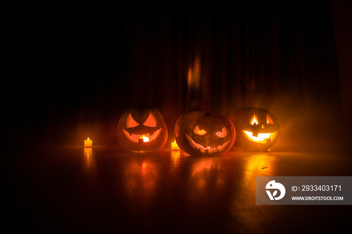 Halloween pumpkin head jack o lantern with glowing candles on background. Pumpkins on wooden floor