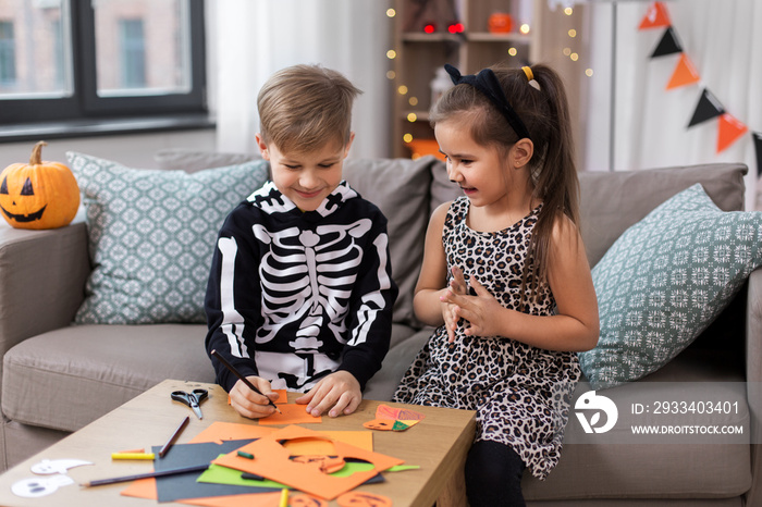 halloween, holiday and childhood concept - smiling little boy and girl in party costumes doing craft