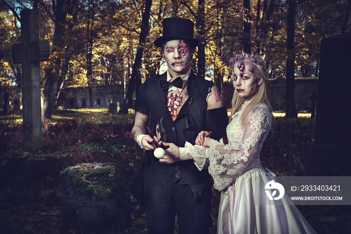 Dressed in wedding clothes romantic zombie couple walking on the abandoned cemetery.