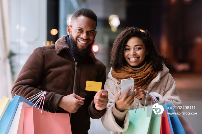 Portrait of happy afro couple using smartphone holding credit card