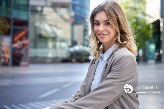 Portrait of smiling woman in office suit, sitting outdoors, looking confident