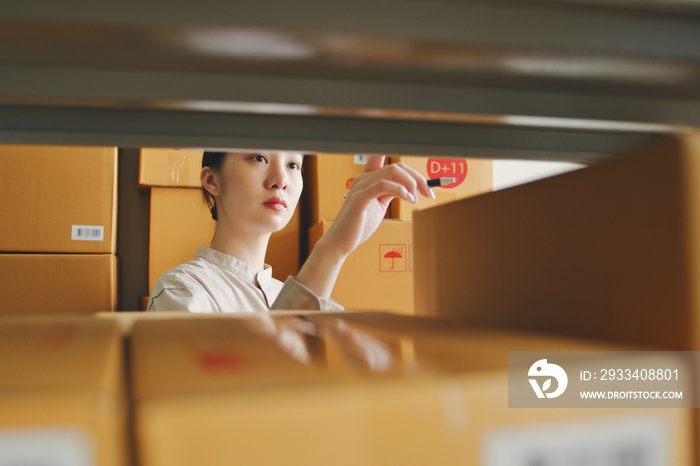 Asian woman working at online store warehouse checking inventory stock parcel boxes on shelves, onli