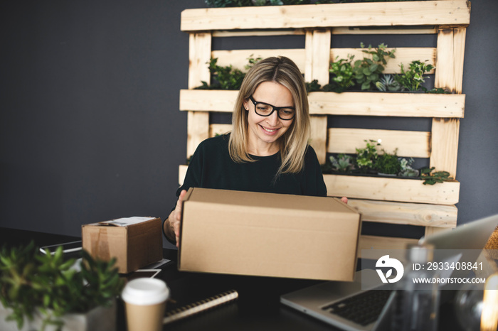 pretty young blonde woman with brown parcels is sitting in front of laptop in a very modern, ecologi