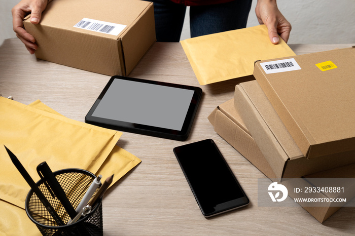 Delivery person working,checking parcels on the workplace.Pile of boxes,padded mailers,tablet pc,sma