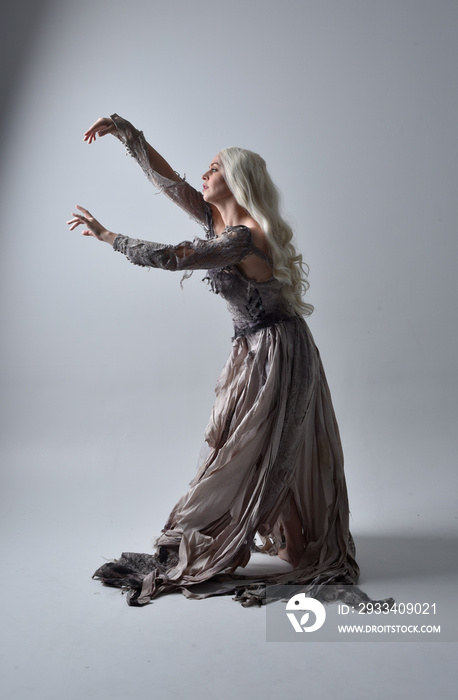 full length portrait of girl wearing old torn wedding dress. standing pose with rim lighting on a gr