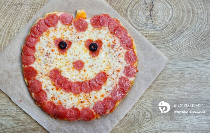 Chuck E. Cheese Pumpkin Pizza on parchment paper with wooden background.Creative art food idea for c