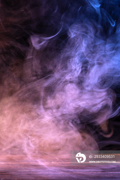 Conceptual image of multi-colored smoke isolated on dark black background and wooden table.