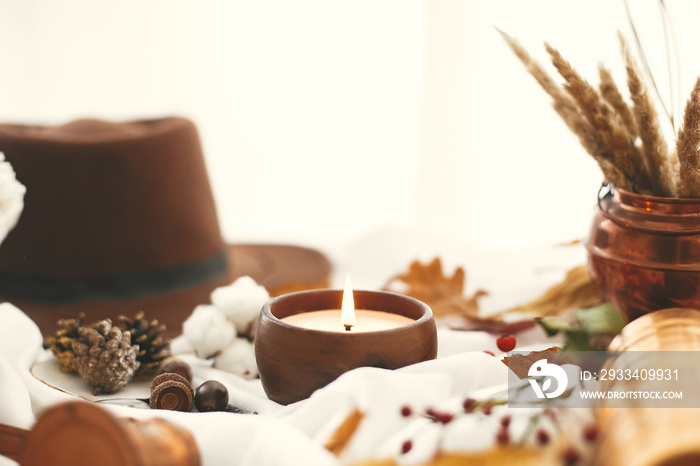 Hygge lifestyle. Candle, berries, fall leaves, herbs, acorns, nuts and brown hat on white fabric. Au