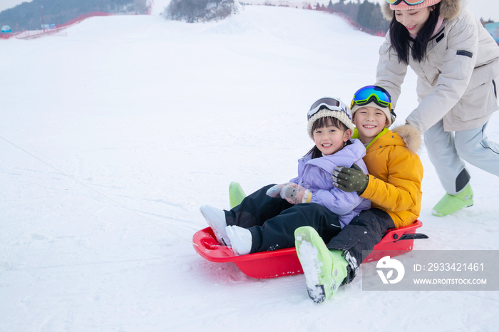 雪场上妈妈推着坐在雪上滑板的孩子们