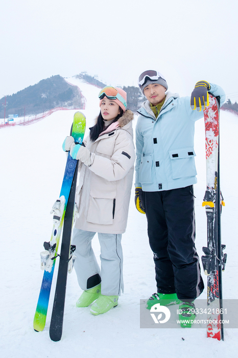 青年伴侣扶着滑雪板站在雪地上