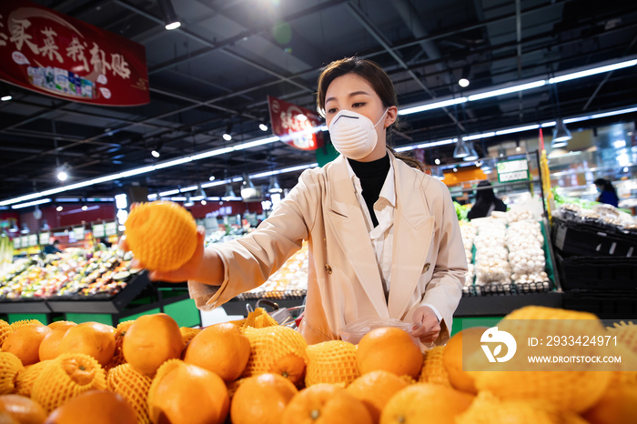 戴口罩的青年女人在超市挑选水果